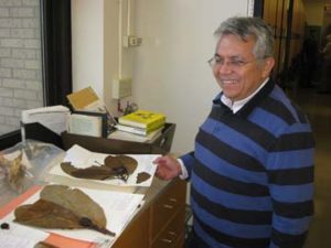 a smiling man holds a herbarium specimen